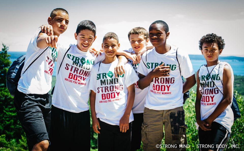 Diverse group of young men in Strong Mind Strong Body shirts celebrating on a hilltop